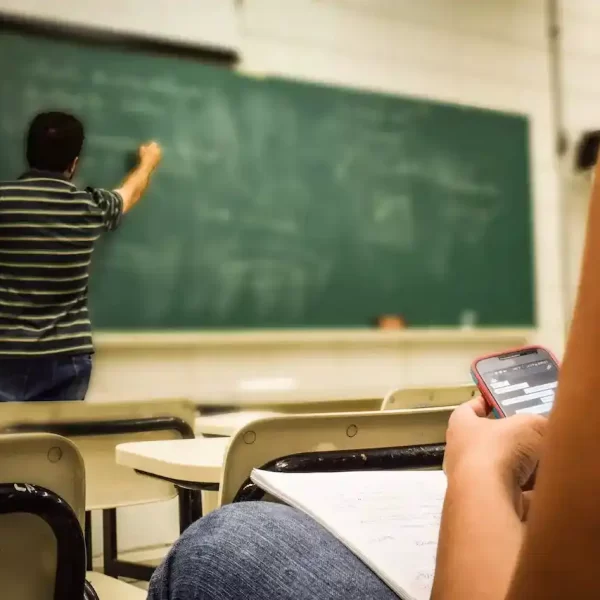 A student looking in their cellphone with the teacher is teaching in front of the class