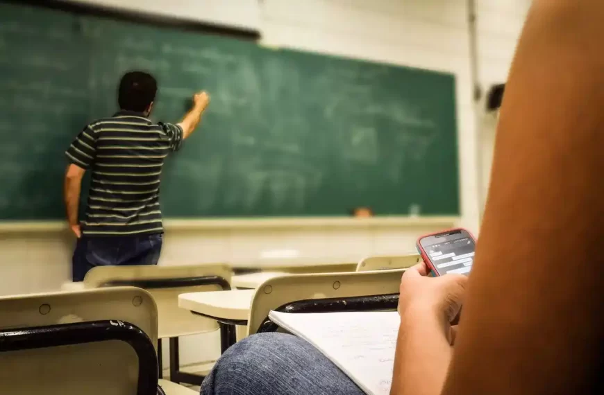 A student looking in their cellphone with the teacher is teaching in front of the class