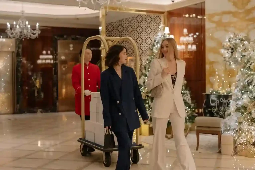 Two girls walking in blazers with their luggage being pushed behind by a man in a luxurious hotel