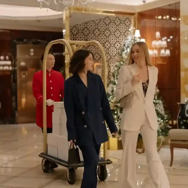 Two girls walking in blazers with their luggage being pushed behind by a man in a luxurious hotel