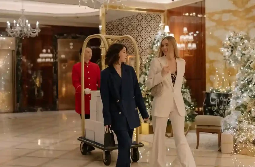 Two girls walking in blazers with their luggage being pushed behind by a man in a luxurious hotel