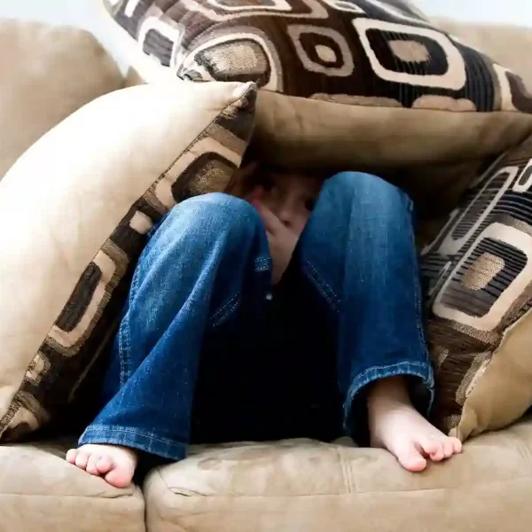 A person hiding under the pillows on a couch