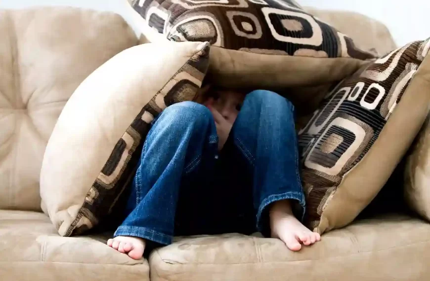 A person hiding under the pillows on a couch