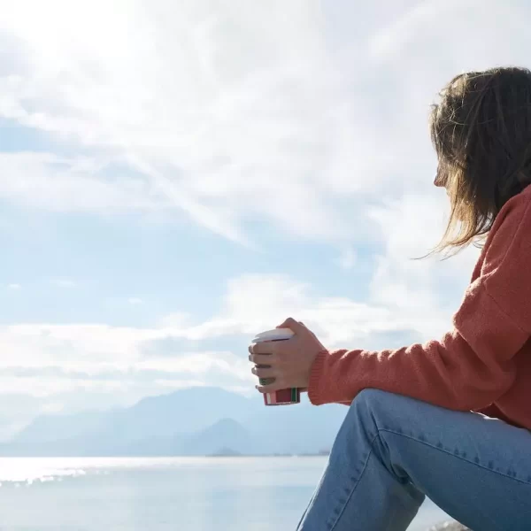 A girl sitting by the water with coffee in her hand just thinking deeply