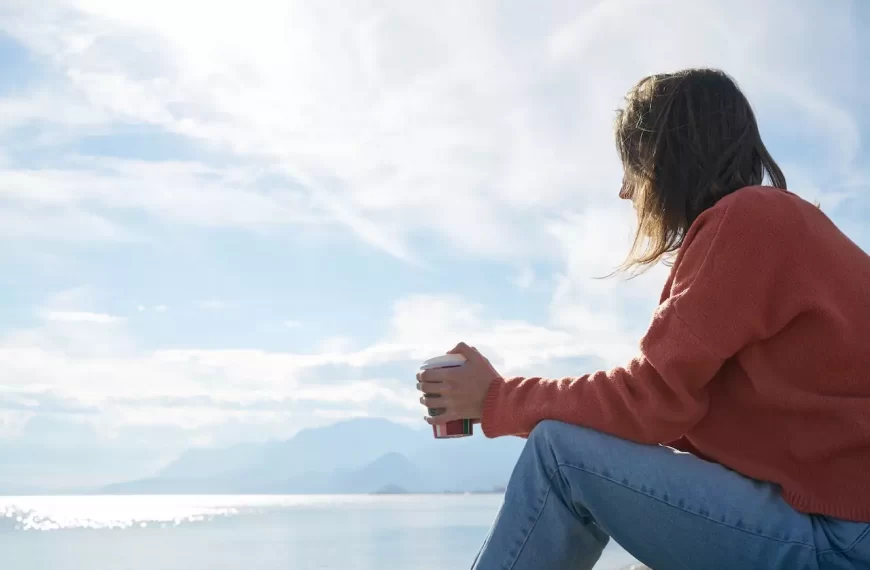 A girl sitting by the water with coffee in her hand just thinking deeply