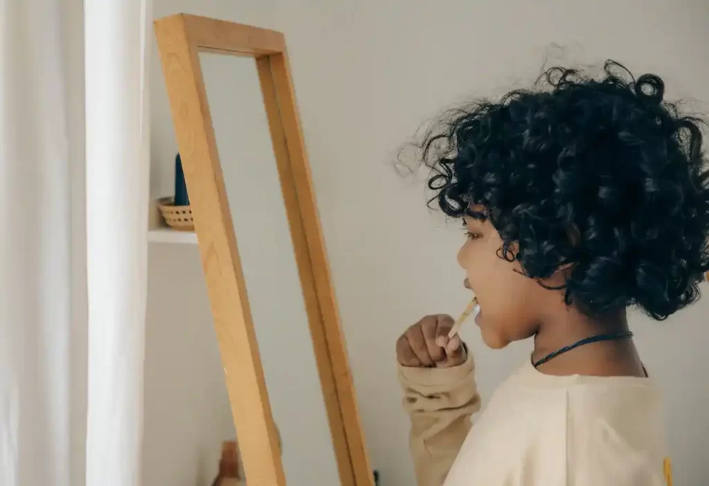 A kid brushing his teeth in front of the mirror