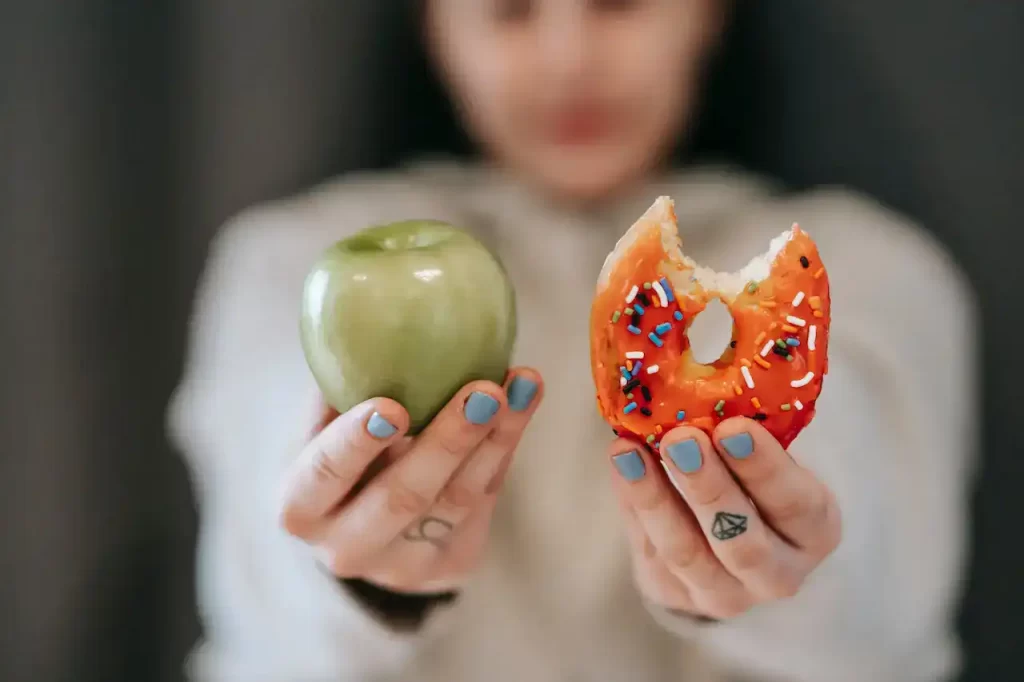 A girls holding a donut and a apple in front of her