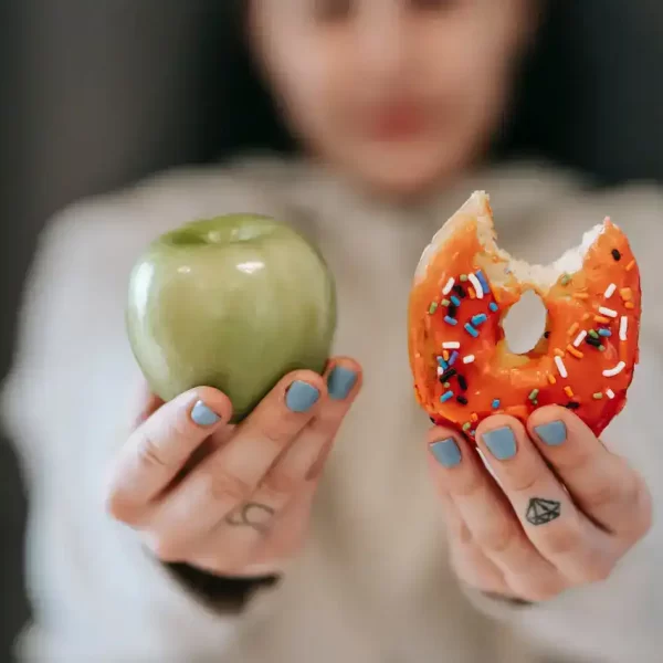 A girls holding a donut and a apple in front of her