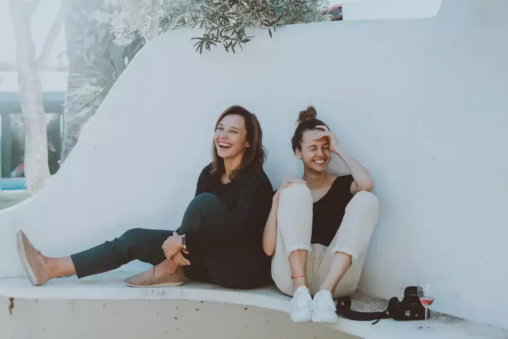 2 women sitting on a white bench laughing