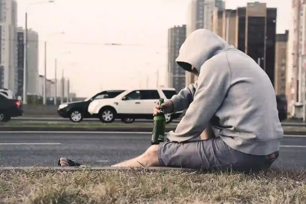 A man sitting on the side of the road with a bottle of alcohol in his hand