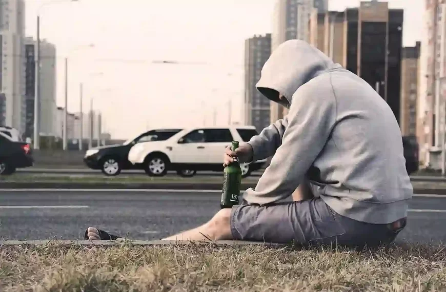 A man sitting on the side of the road with a bottle of alcohol in his hand