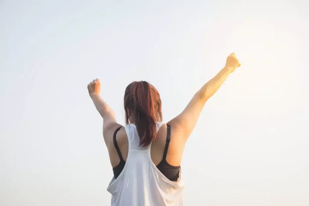 A woman in black and white tank top raising both her arm to the top