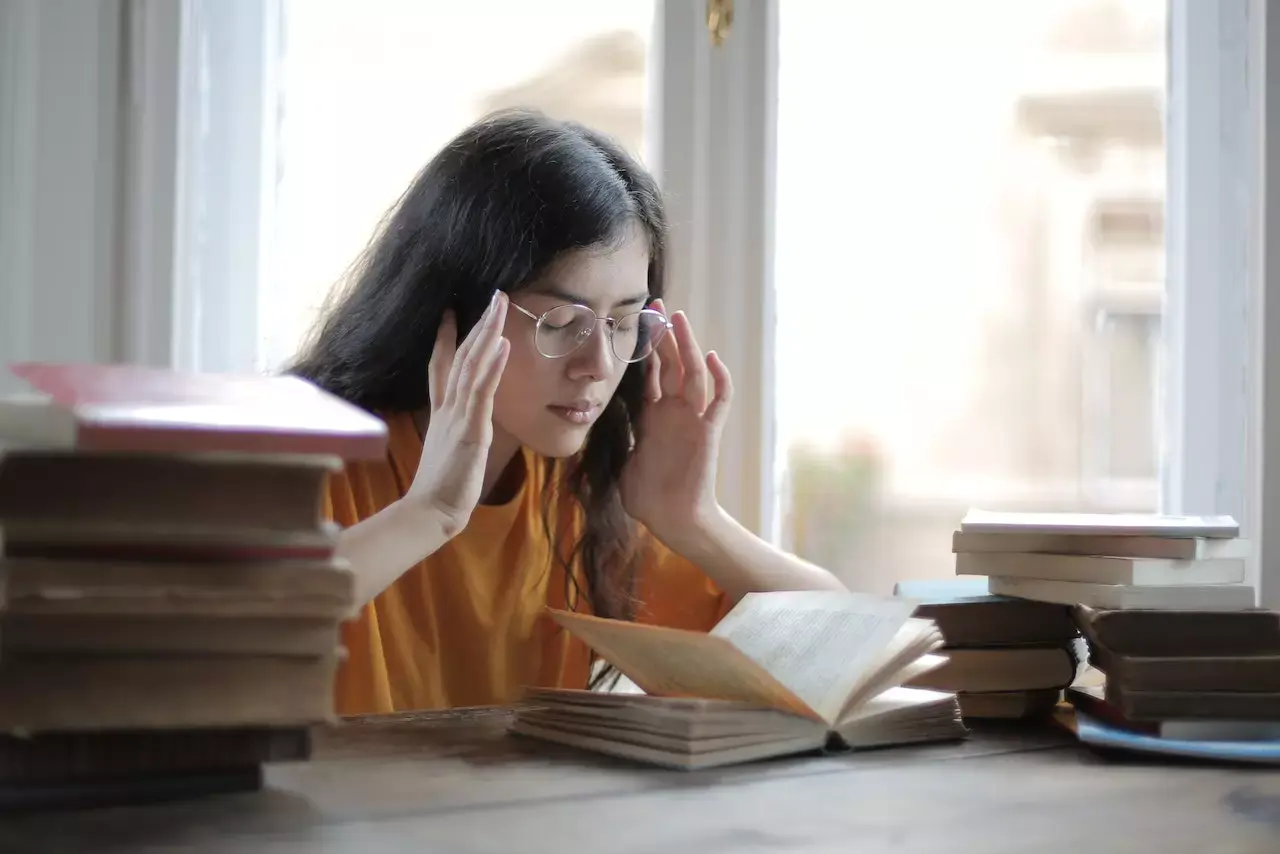 A woman sitting with a bunch of books thinking