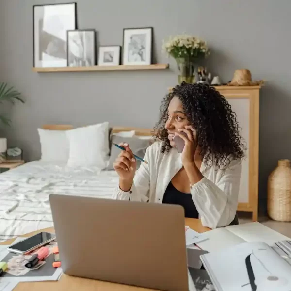 A woman sitting in front of a computer while talking on the phone, with a pen in her hand