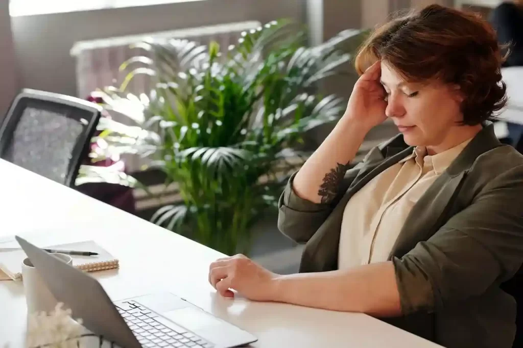 A woman holding her head while sitting in front of the Pc