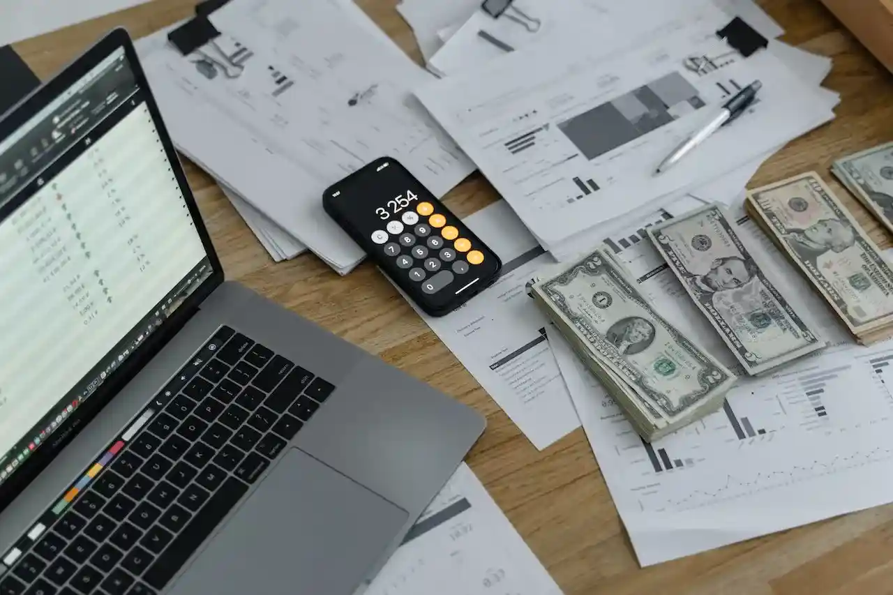 a table with money, phone, and a laptop with excel sheet on it