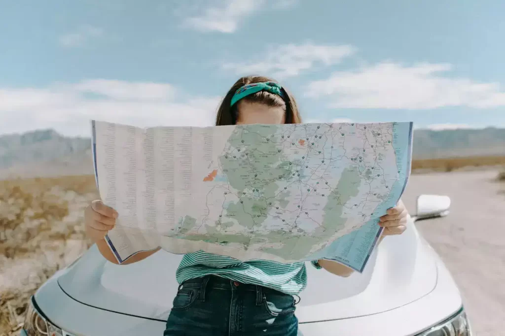 A woman sitting on the hood of a car and looking at the map