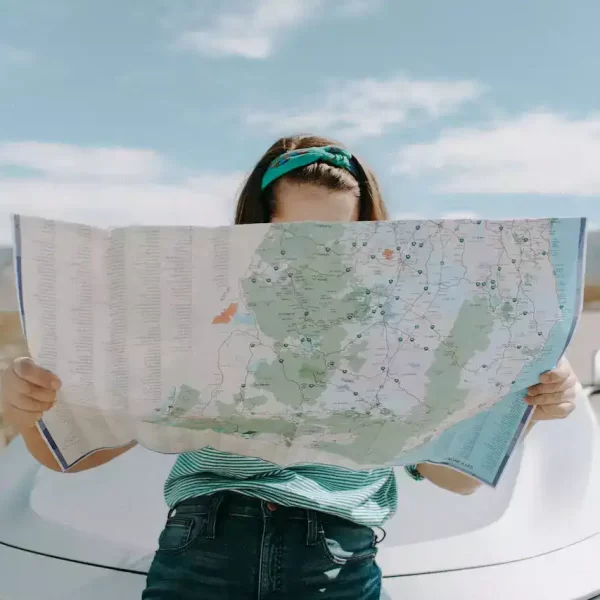 A woman sitting on the hood of a car and looking at the map