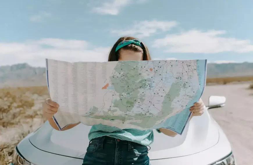 A woman sitting on the hood of a car and looking at the map