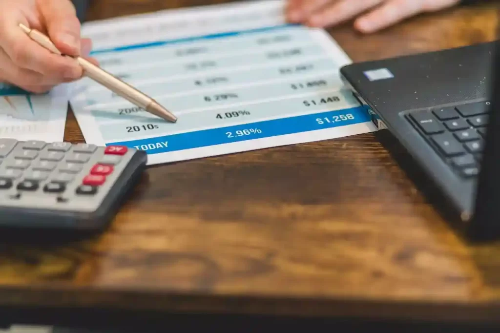 a hand showing interest rates on a paper with a calculator and a laptop besides it