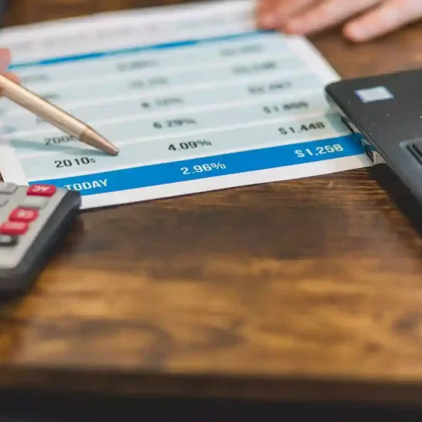 a hand showing interest rates on a paper with a calculator and a laptop besides it