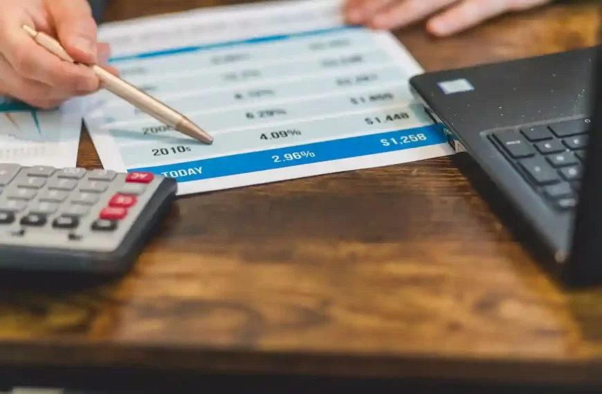 a hand showing interest rates on a paper with a calculator and a laptop besides it