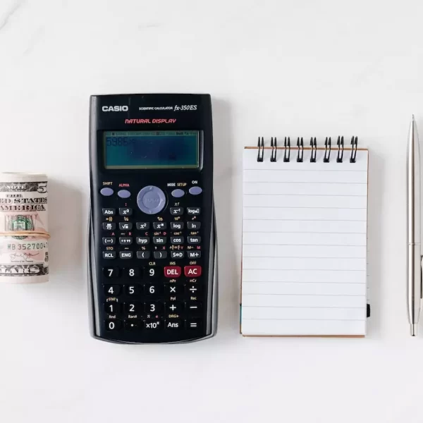 A calculator, notepad, pen, and a roll of cash on a table