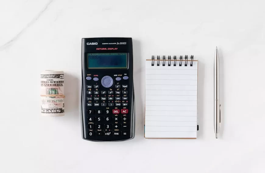 A calculator, notepad, pen, and a roll of cash on a table