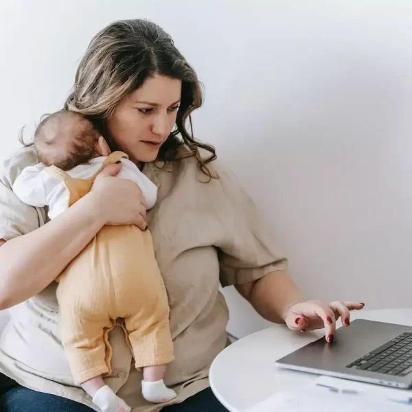 Young working mother cuddling her baby and using laptop at home