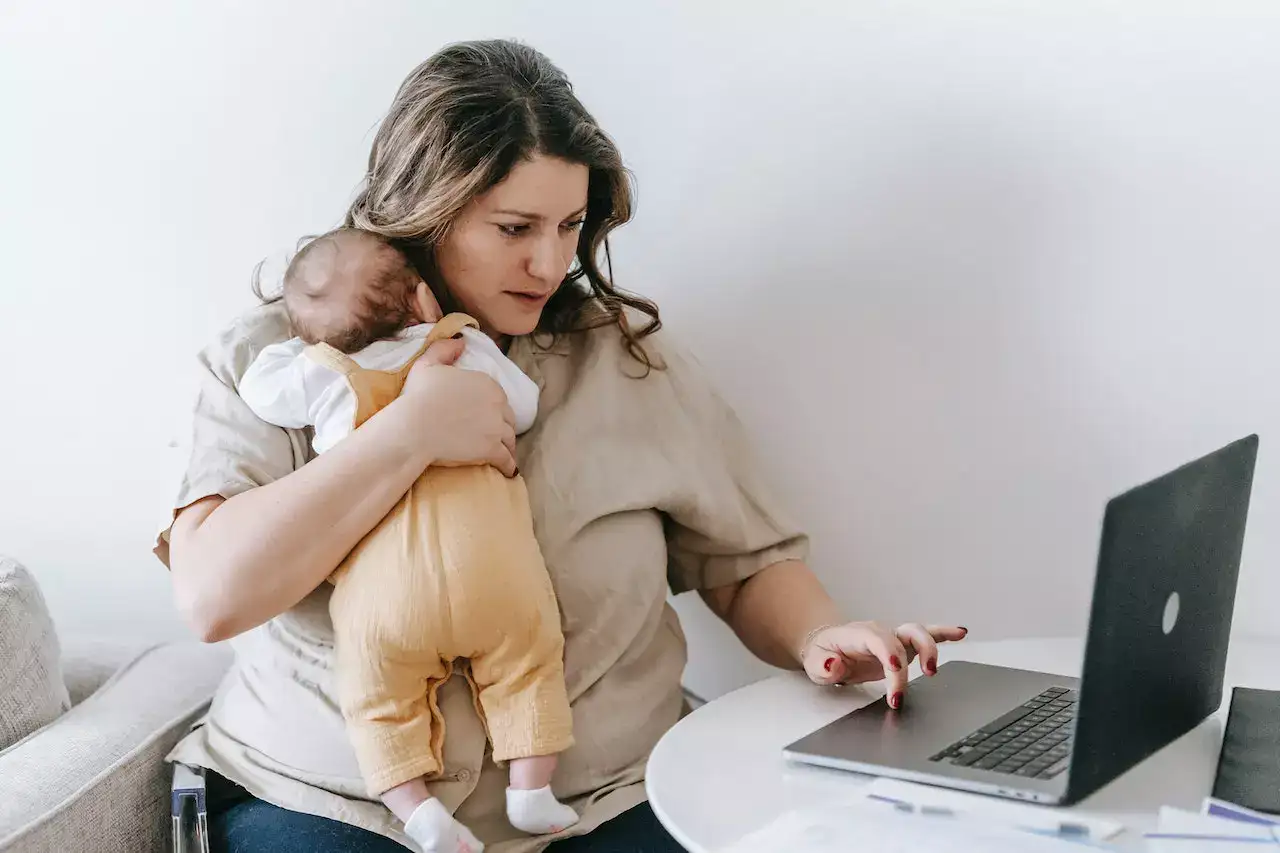 Young working mother cuddling her baby and using laptop at home