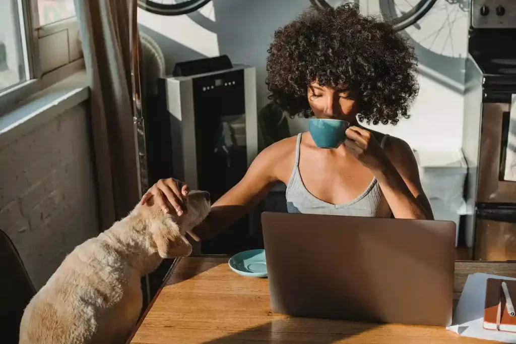 A female freelancer using laptop and drinking coffee while also petting a dog