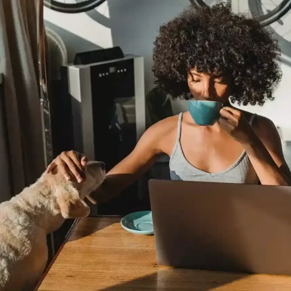 A female freelancer using laptop and drinking coffee while also petting a dog