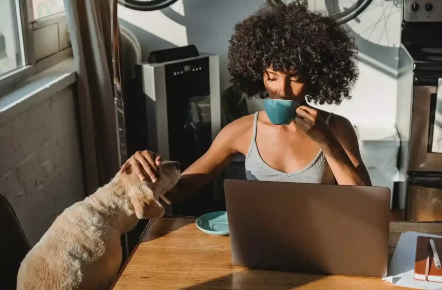 A female freelancer using laptop and drinking coffee while also petting a dog