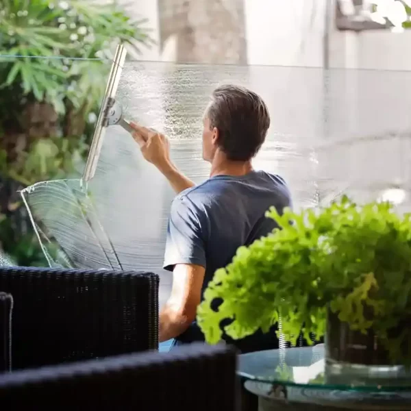 Man in gray shirt cleaning clear glass near a sofa