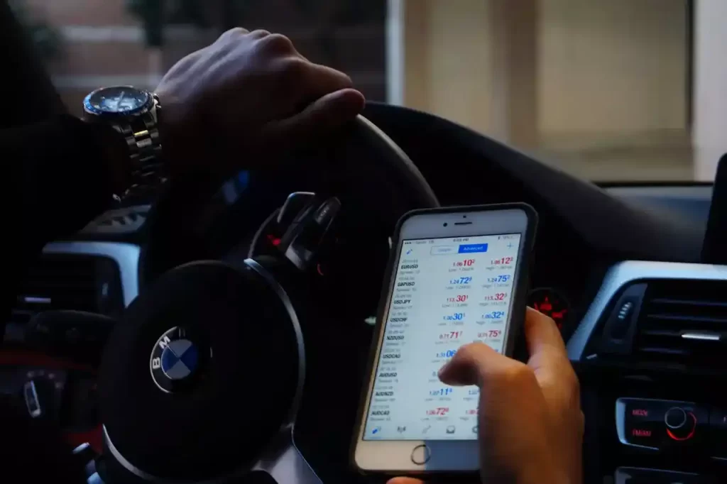 A guy in a car looking at his phone with trading app