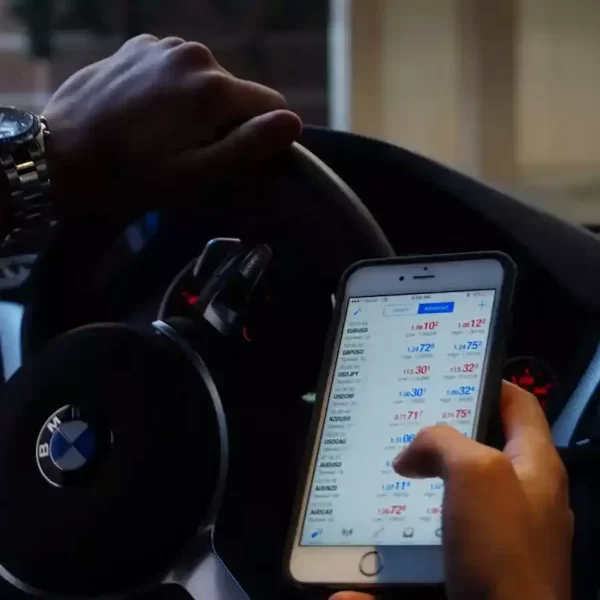 A guy in a car looking at his phone with trading app