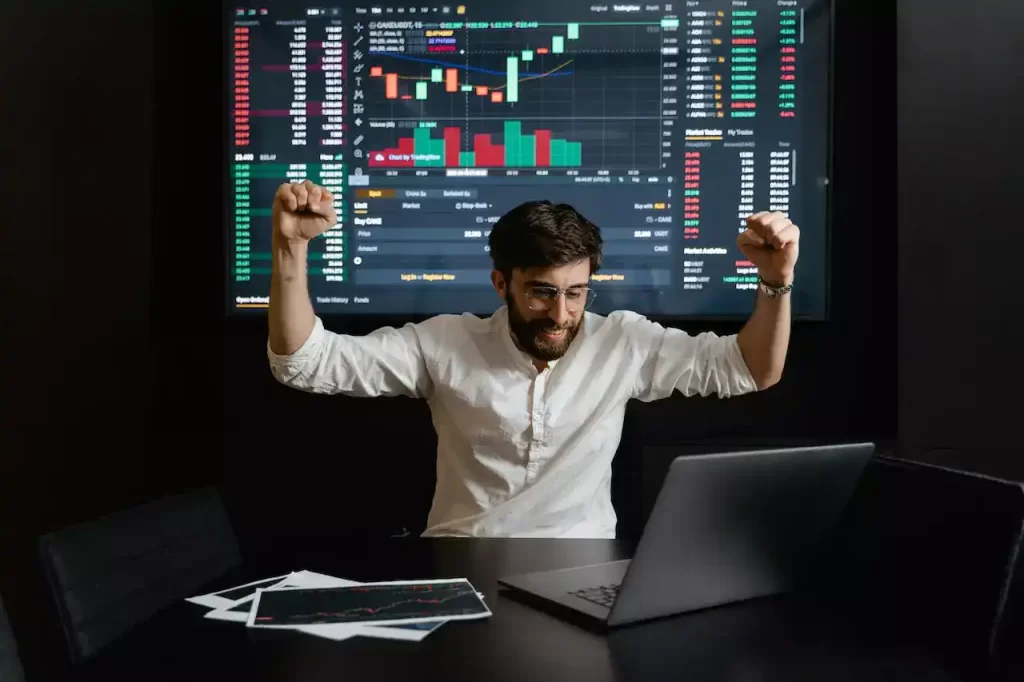 A man raising his hands for being being successful with a trading chart projected behind him