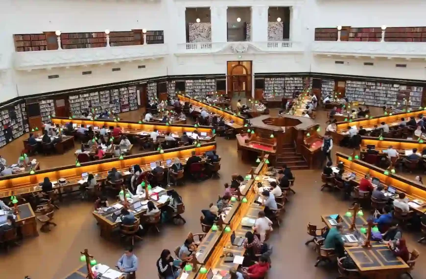 Many people sitting inside a room that looks like a library, looking at computers