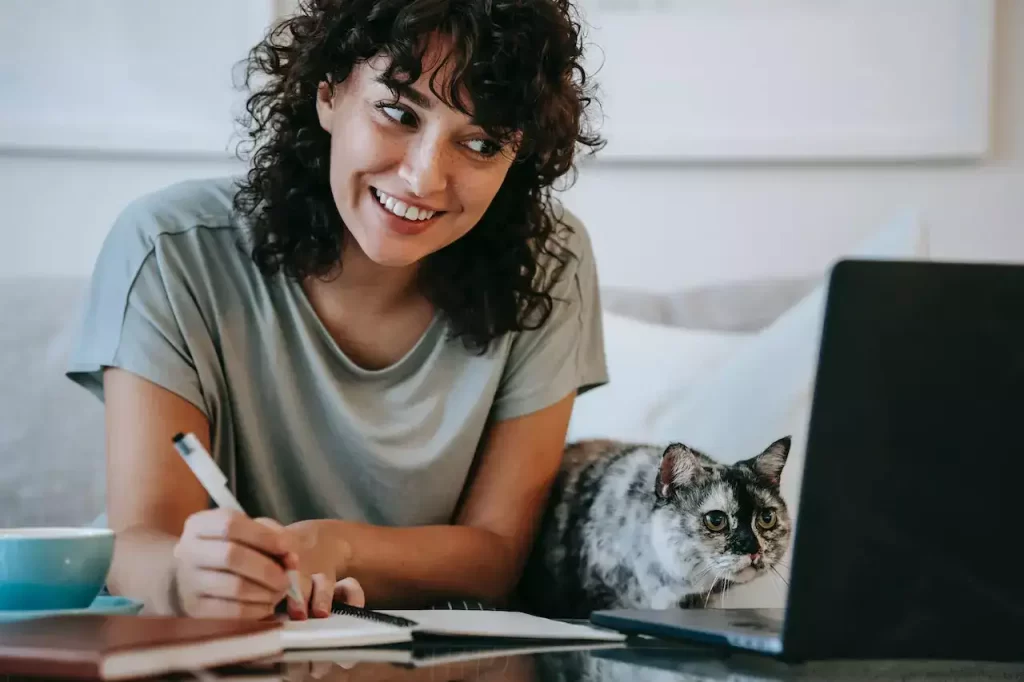 A woman writing in her planner with a cat sitting besides her