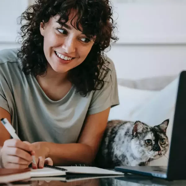 A woman writing in her planner with a cat sitting besides her