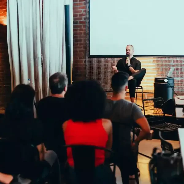 A man speaking on a small stage with people listening attentively