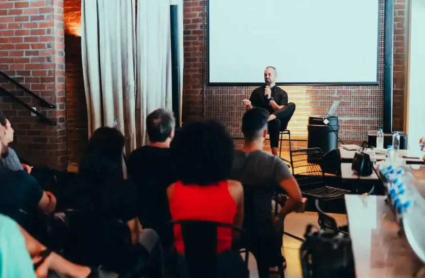 A man speaking on a small stage with people listening attentively