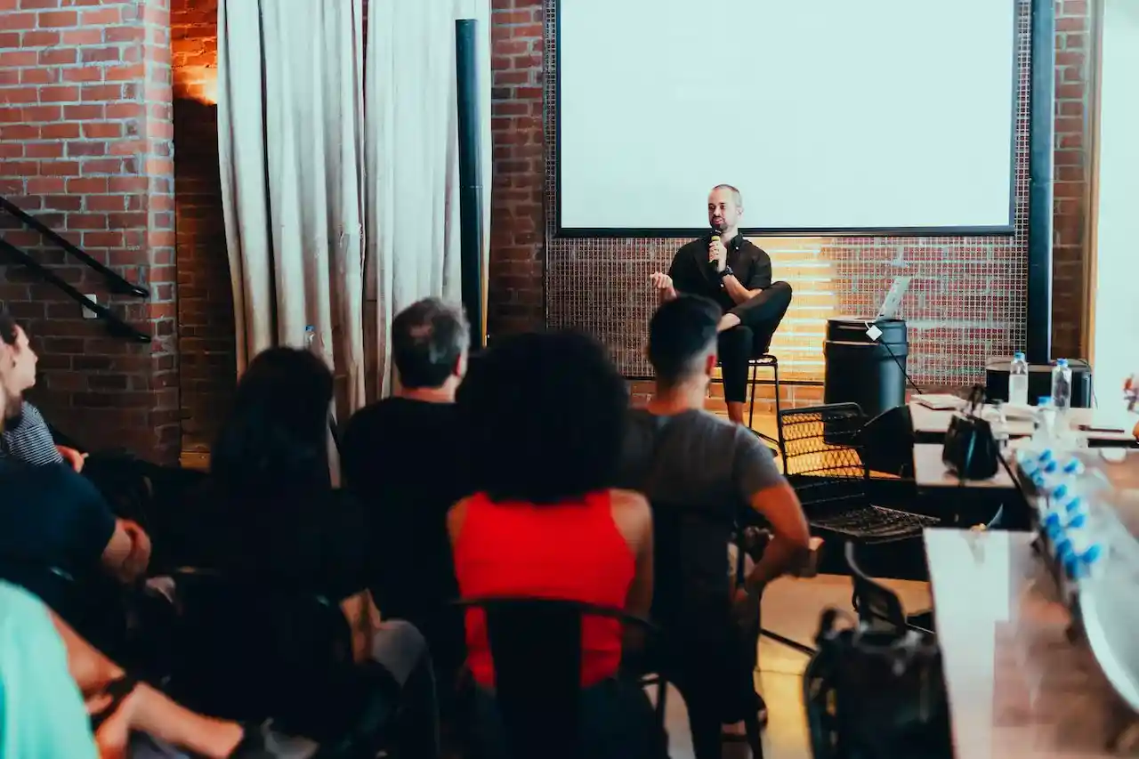 A man speaking on a small stage with people listening attentively