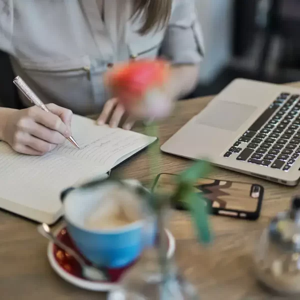 A woman writing in a notebook in front of a laptop