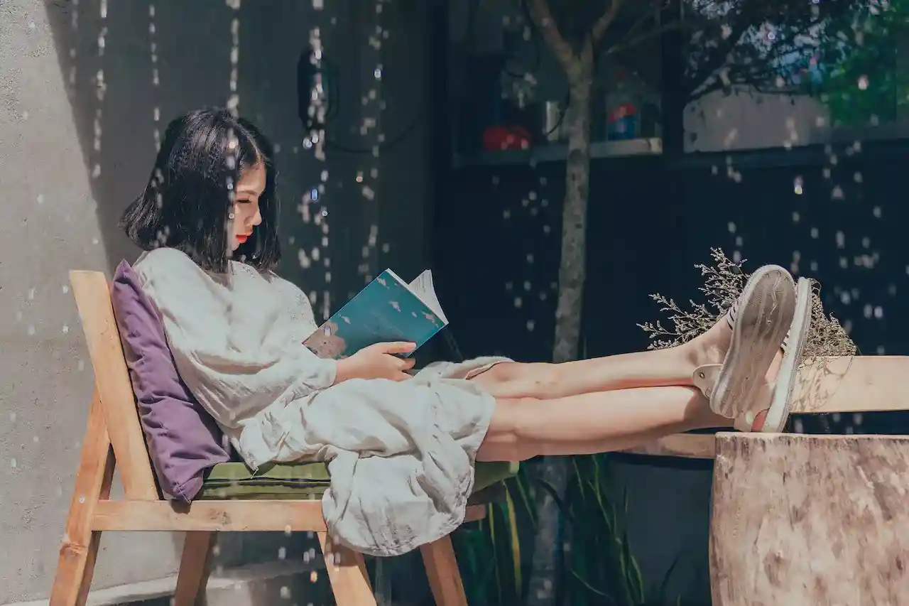 a sitting on a chair with her feet on the table, reading a book