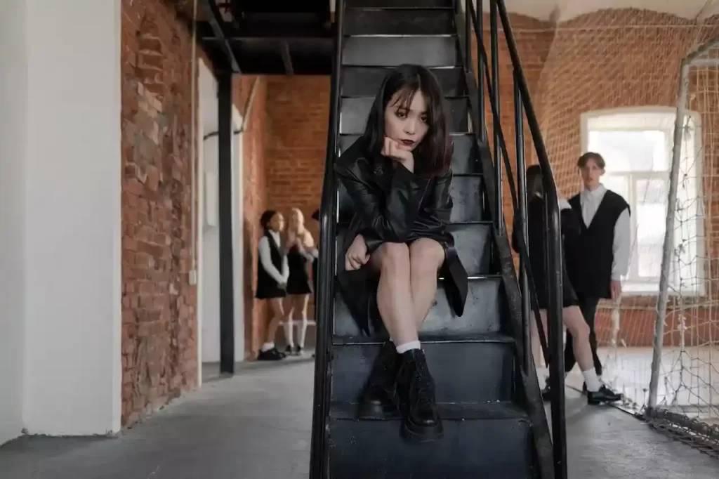 Teen girl with a black leather jacket sitting on a black staircase looking at the camera