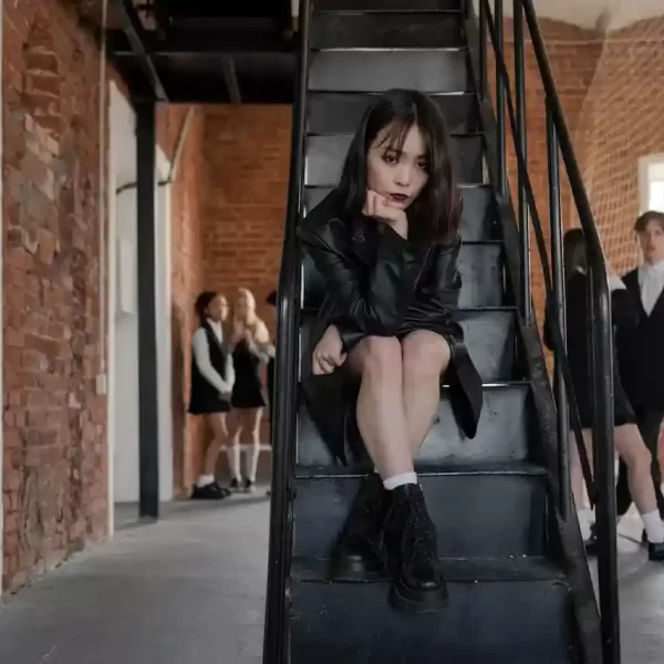 Teen girl with a black leather jacket sitting on a black staircase looking at the camera