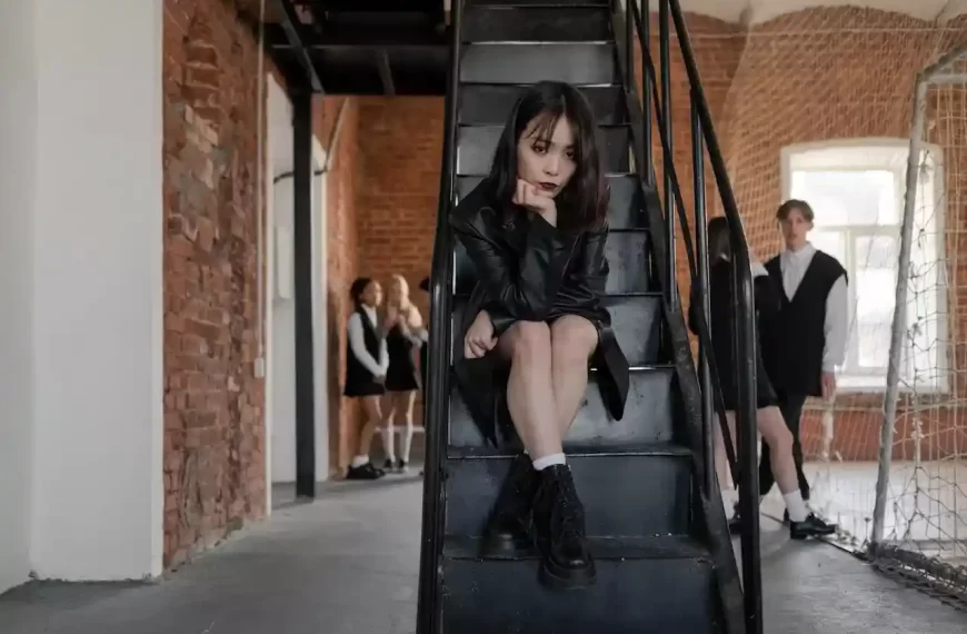 Teen girl with a black leather jacket sitting on a black staircase looking at the camera