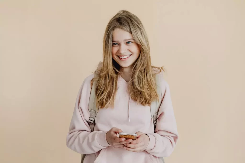 A young woman in pink sweater smiling while holding her phone