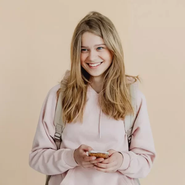 A young woman in pink sweater smiling while holding her phone
